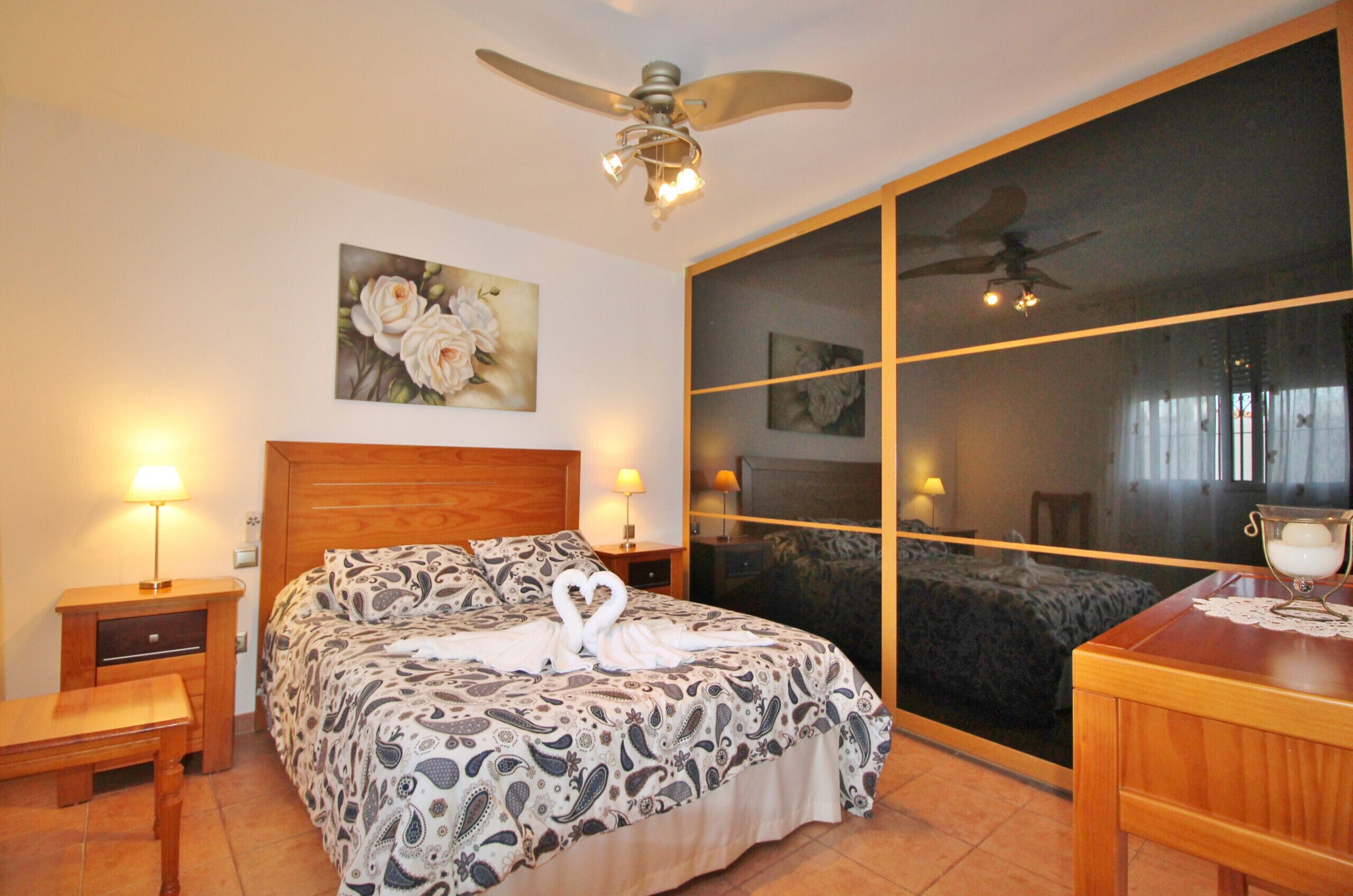 Ein Schlafzimmer mit Bett, Nachttischen, Deckenventilator und einem großen Fenster.