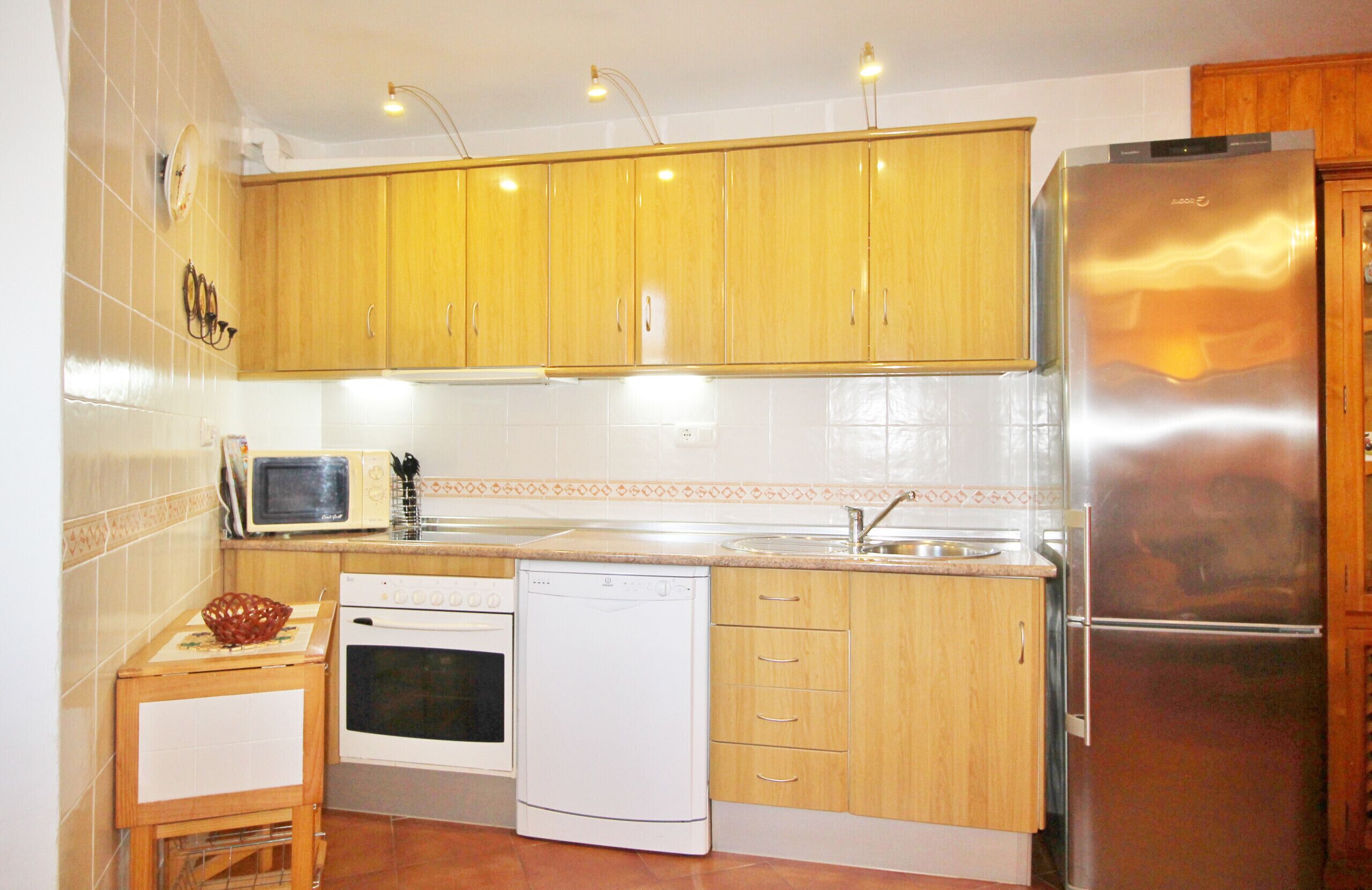 A compact kitchen with wooden cabinets, a stainless steel refrigerator, a microwave, an oven, and a dishwasher.