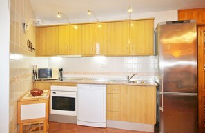 A compact kitchen with wooden cabinets, a stainless steel refrigerator, a microwave, an oven, and a dishwasher. - 1010 Apartment Kika (Nerja)