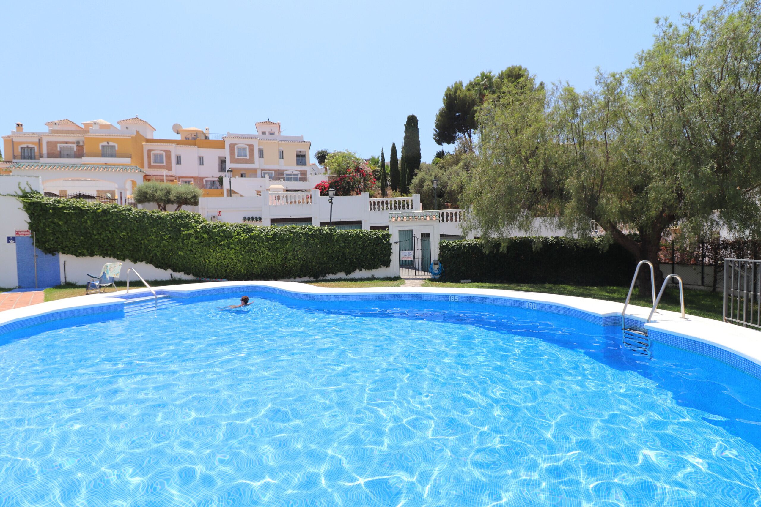 Una piscina con agua cristalina, rodeada por una valla blanca, y edificios al fondo.
