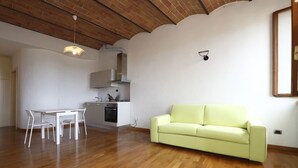 Ein großzügiger Wohnbereich mit Esstisch und Stühlen, einem hellgrünen Sofa und einer Küche im Hintergrund.