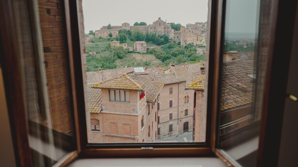 Blick durch ein Fenster auf eine Stadtlandschaft mit historischen Gebäuden und einer Burg auf einem Hügel.