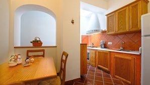 A compact kitchen with wooden cabinets, a tiled backsplash, and a dining area with a table and chairs. - White Daisy is a small villa on two floors (Praiano)