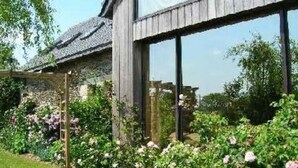 A rustic wooden building with large windows, surrounded by lush greenery and flowering plants. - mansion - 3 rooms - 6 persons (Taulé)