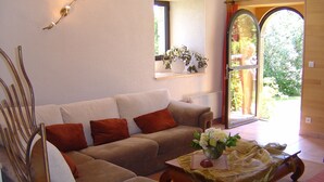 A living room with a sofa, a coffee table, and a chair. There is a window with a view of greenery outside. - mansion - 3 rooms - 6 persons (Taulé)
