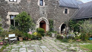 A stone building with a paved courtyard, potted plants, and a wooden chair. - mansion - 3 rooms - 6 persons (Taulé)