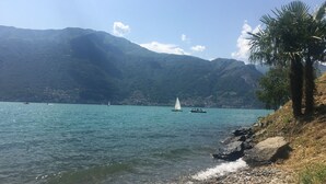 A lake with boats, a rocky shoreline, and mountains in the background. - Fantastic apartment with a wonderful panoramic view of Lake Como  (Dorio)
