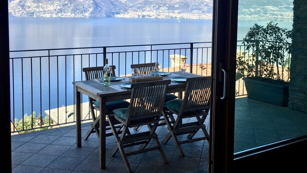 A dining area with a table and chairs, a potted plant, and a view of a lake with mountains in the background. - Fantastic apartment with a wonderful panoramic view of Lake Como  (Dorio)