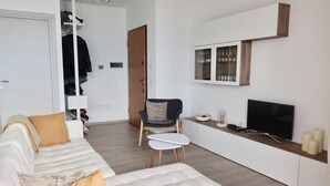 A modern living room with a white sofa, a small table, a chair, a TV, and a cabinet with glass doors. - Fantastic apartment with a wonderful panoramic view of Lake Como  (Dorio)