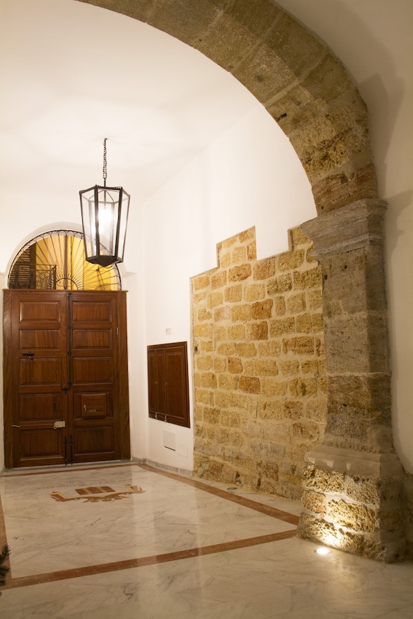 A hallway with a stone wall, a wooden door, and a hanging light fixture.