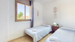 Ein Zimmer mit zwei Einzelbetten, einem Fenster mit Vorhängen, einem Nachttisch mit Lampe und einer kleinen Pflanze.