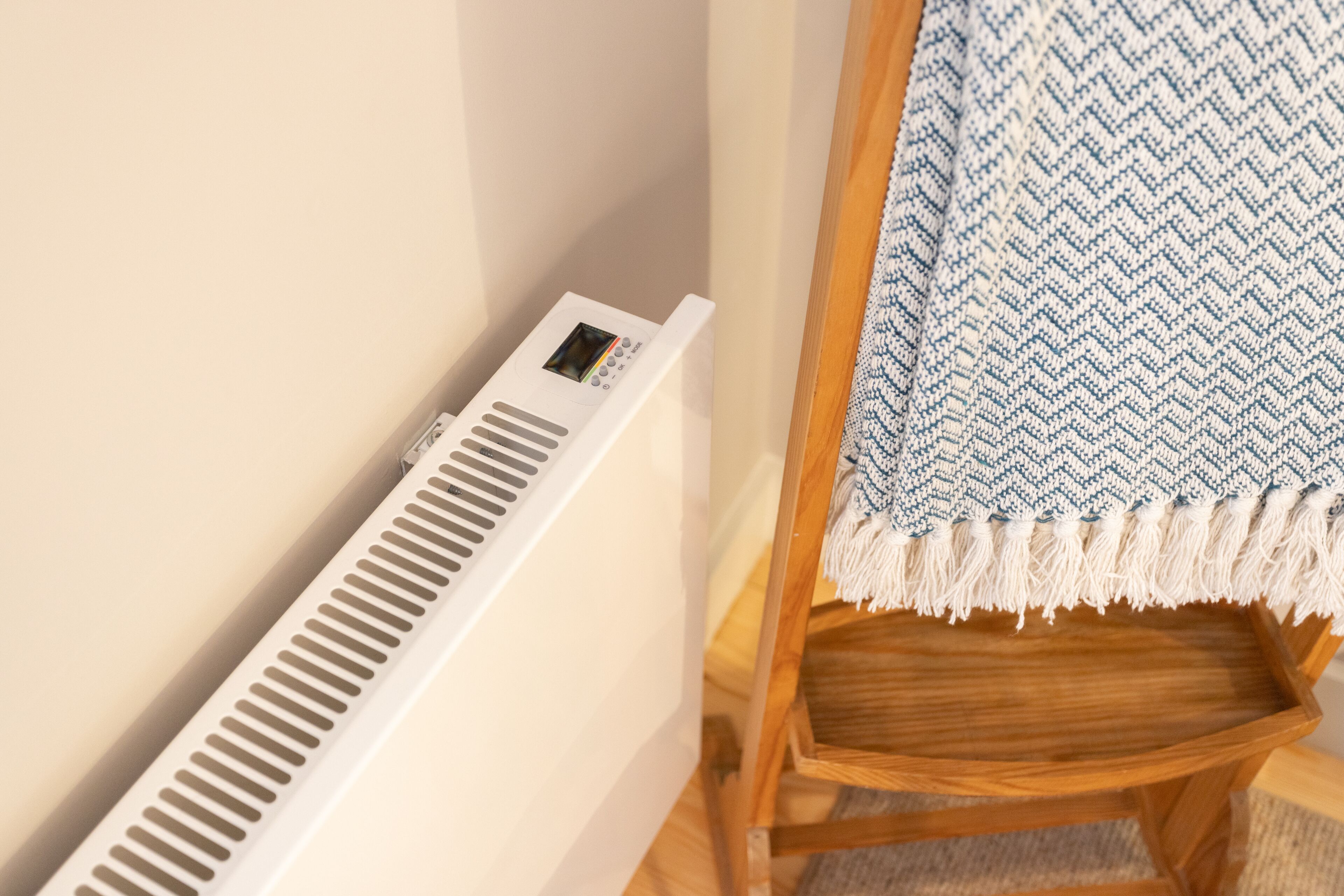 A corner of a room with a white vent, a wooden chair, and a blue and white patterned rug.