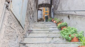 A narrow stone staircase with potted plants on the sides, leading to a door at the top.