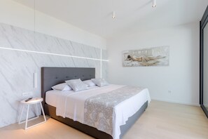 A modern bedroom with a marble wall, a large bed, a bedside table, and a painting on the wall.