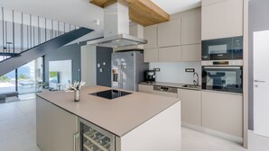 Een moderne keuken met een centraal eiland, inbouwapparatuur en een trap naar een buitenruimte.