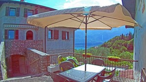 A balcony with a table and chairs, a large beige umbrella, and a scenic view of a mountainous landscape.
