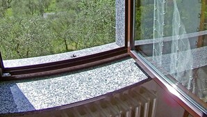 A room with a large window offering a view of a green landscape with trees and a building in the distance.