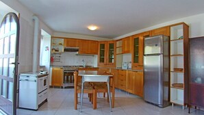 A compact kitchen with wooden cabinets, a stainless steel refrigerator, a stove, and a dining table with chairs.