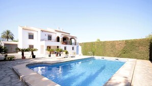 A pool area with a white building, a concrete deck, and a stone wall.