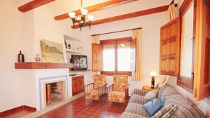 A cozy living room with a fireplace, a sofa, floral armchairs, and a television.