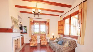 A spacious living room with a fireplace, a sofa, two armchairs, and a television.