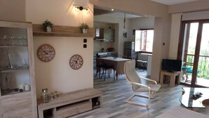 A spacious living area with a wooden floor, a dining table, a TV, and a balcony with outdoor seating. - VILLA SOFIA (ground floor self - contained apartment) (Marathos)