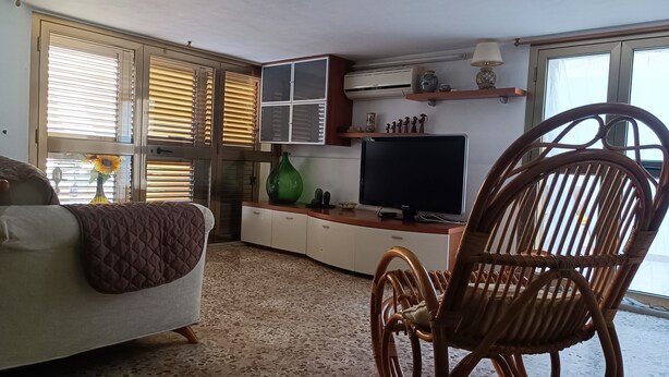 A living room with a sofa, a wicker chair, a television, and a cabinet.