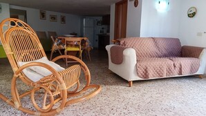 A living room with a wicker rocking chair, a white sofa, and a dining area with a table and chairs.