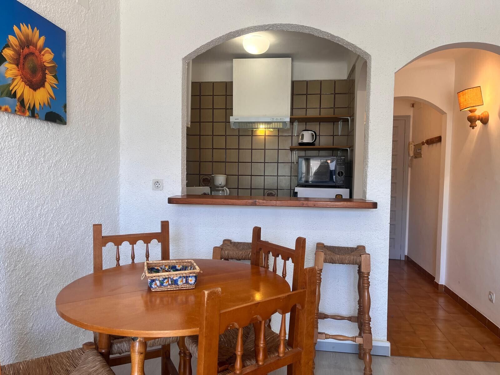 A dining area with a wooden table and chairs, a kitchen with a microwave and kettle, and a tiled backsplash.