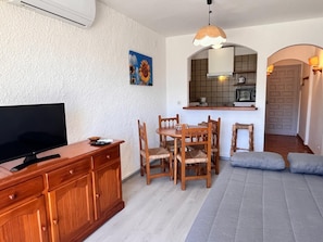 A compact living space with a TV, wooden dining table, chairs, a sofa, a kitchen area with a microwave, and a door with a patterned design. - 0167-POBLAT TIPIC Studio near the beach (Empuriabrava)