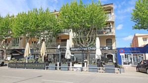 A street view with outdoor seating areas, a restaurant named "La Bateria," and a building with balconies. - 0167-POBLAT TIPIC Studio near the beach (Empuriabrava)