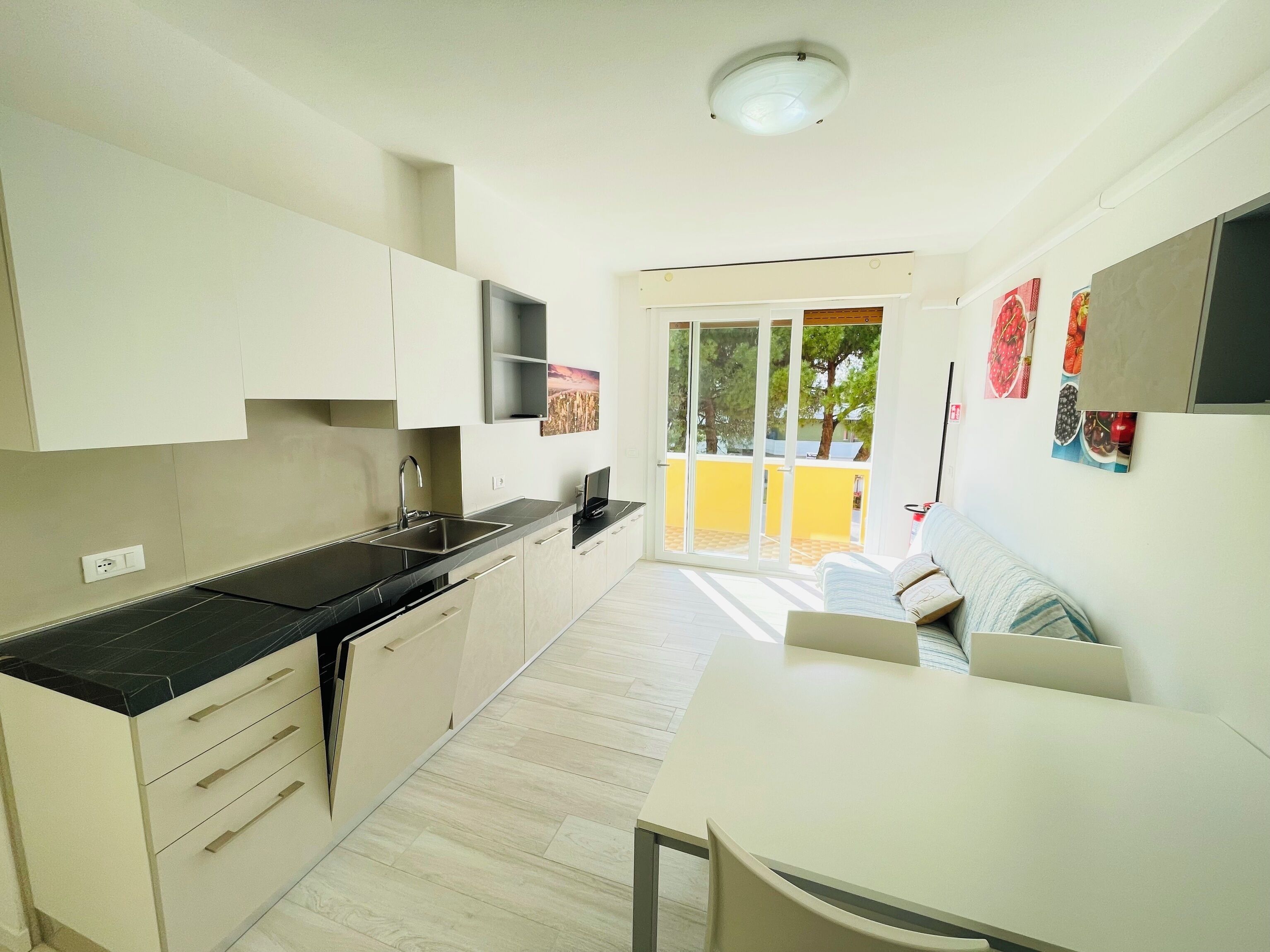 A modern kitchen with a dining area, a TV, and a sliding door leading to an outdoor space.