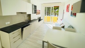 A modern kitchen with a dining area, a TV, and a sliding door leading to an outdoor space. - Cozy apartment with large balcony (Bibione)