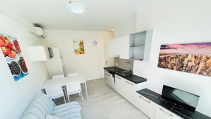A compact living space with a kitchenette, a dining area, a sofa, and a cityscape view. - Cozy apartment with large balcony (Bibione)