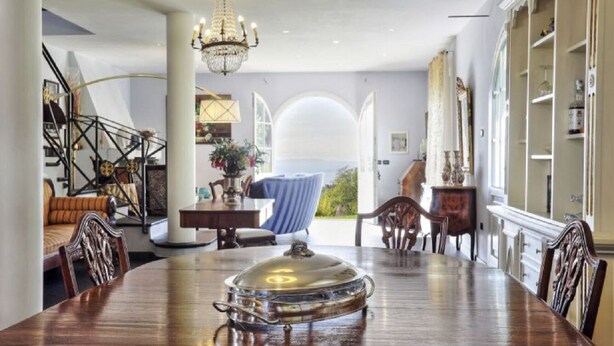 A dining area with a large wooden table, a chandelier, and a view through an arched window. - Elegant Villa near Lucca with big and panoramic garden and private pool (Capannori)