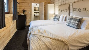 Dormitorio de cabaña de madera con dos camas, un tocador, una cómoda y una pared decorada con estampados de animales.