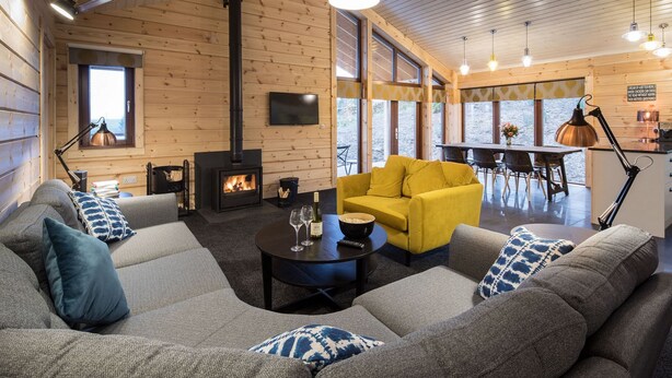 Una sala de estar acogedora con chimenea, un conjunto de sofás, un sillón amarillo y un comedor con mesa y sillas.