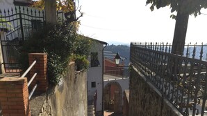 Un escalier en pierre mène à une entrée fermée par un portail et protégée par une clôture en métal, avec une vue sur la mer en arrière-plan.
