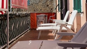 Une terrasse dotée de chaises longues blanches et de parasols à rayures rouges et blanches, de murs en pierre et de volets verts.