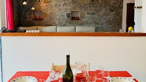 Un coin repas agrémenté d’un mur en pierre, d’une nappe rouge et d’une table mise avec des assiettes, des verres et des couverts.