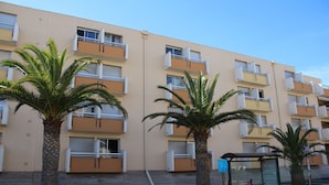 A multi-story building with balconies, palm trees, and a bus stop. - Gites de France Blue by the sea. Free WIFI. (Port-La-Nouvelle)