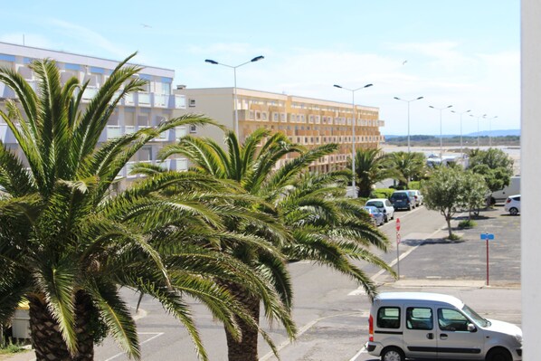 A parking lot with palm trees, a white van, and a building with multiple floors in the background.