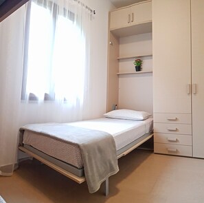 A single bed with a mattress and pillows, a small shelf with a potted plant, and a wardrobe with multiple drawers. - Casa Gina Giardino Holideal Apartment (Tremosine)