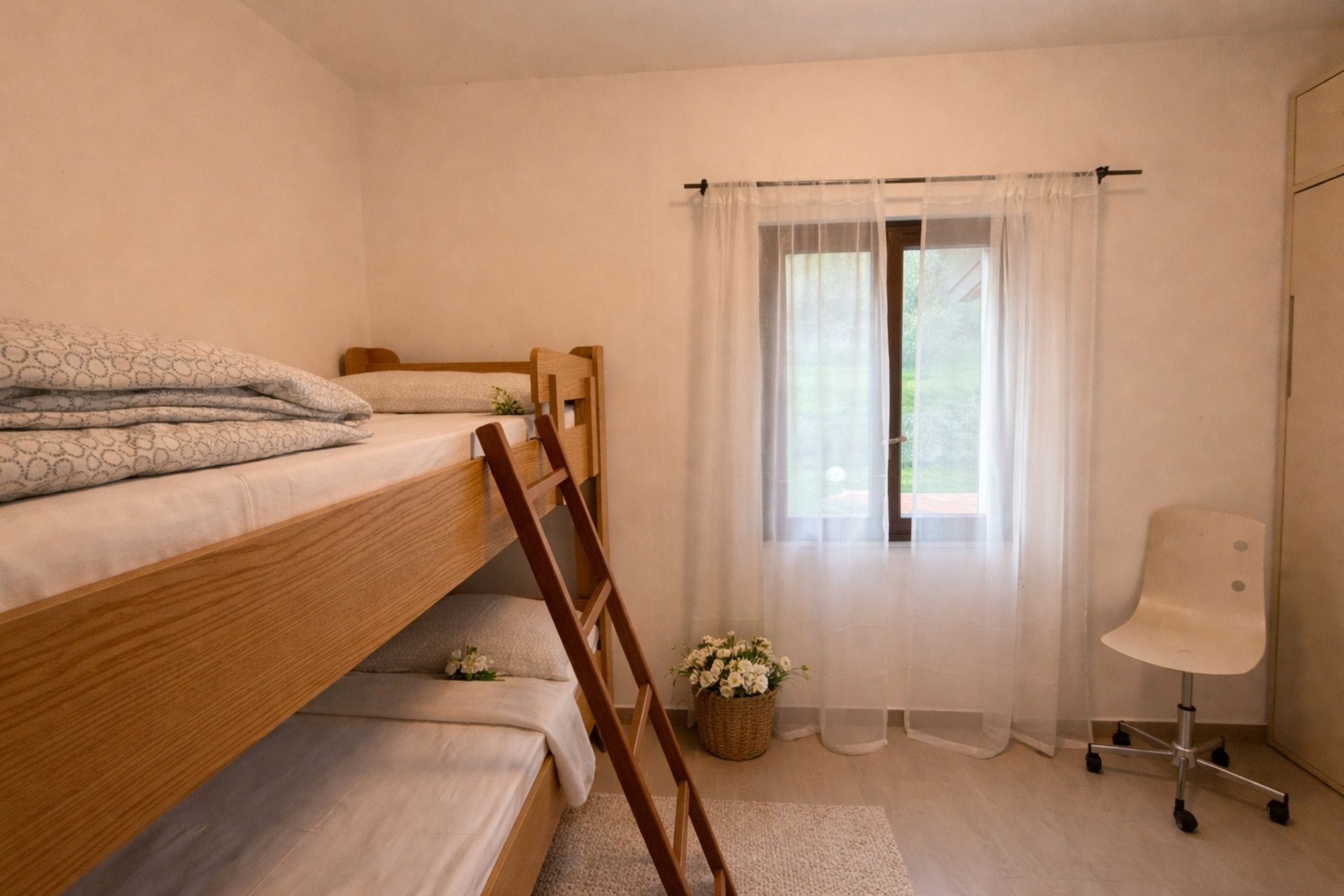 Een slaapkamer met een stapelbed, een bureau, een stoel, een raam met gordijnen en een kleine plant.