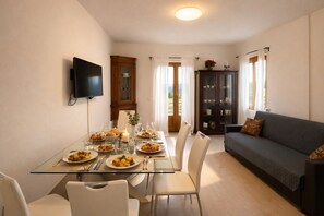 A dining area with a glass table, white chairs, and a dark-colored sofa. - Casa Gina Giardino Holideal Apartment (Tremosine)