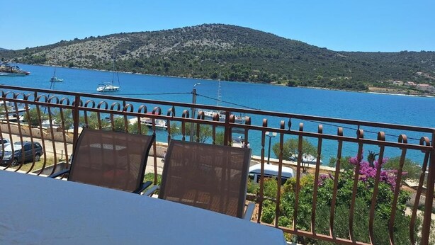 A balcony with a view of a body of water, a mountain in the background, and a railing with flowers.