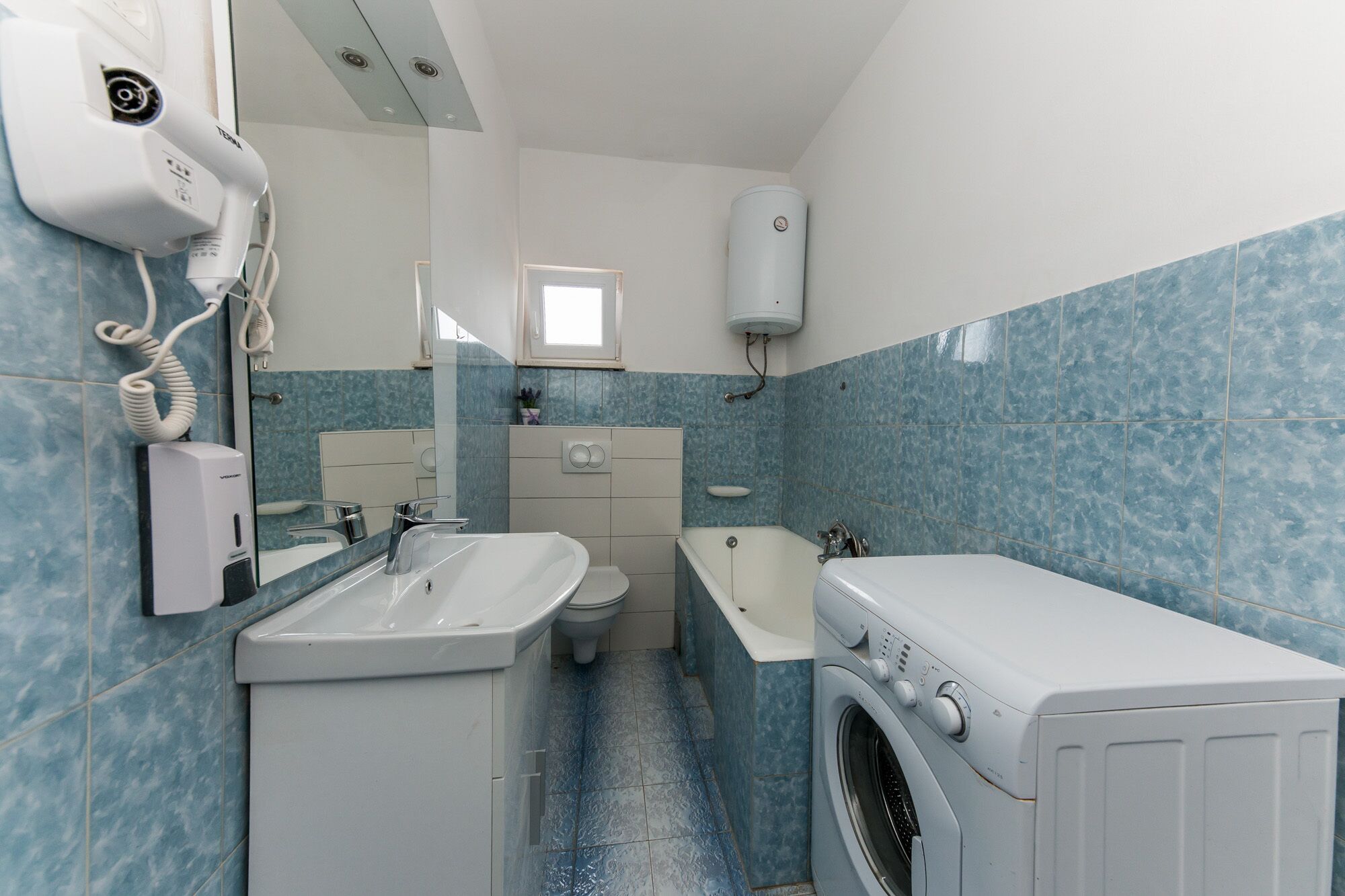 A compact bathroom with a sink, toilet, and washing machine.