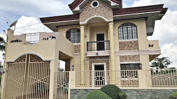 A two-story house with a balcony, a gated entrance, and a stone wall.
