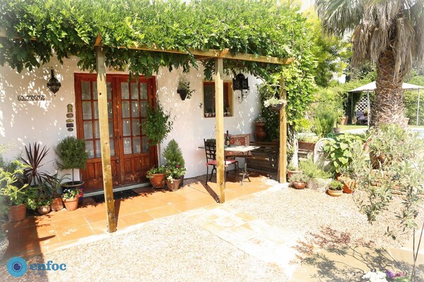 A covered patio with a wooden pergola, potted plants, and a small table and chair.