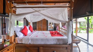 A four-poster bed with a canopy, wooden furniture, and a view of greenery outside. - Fabulous villa right on the beach with large pool, tropical garden & staff (Dencarik/Lovina)